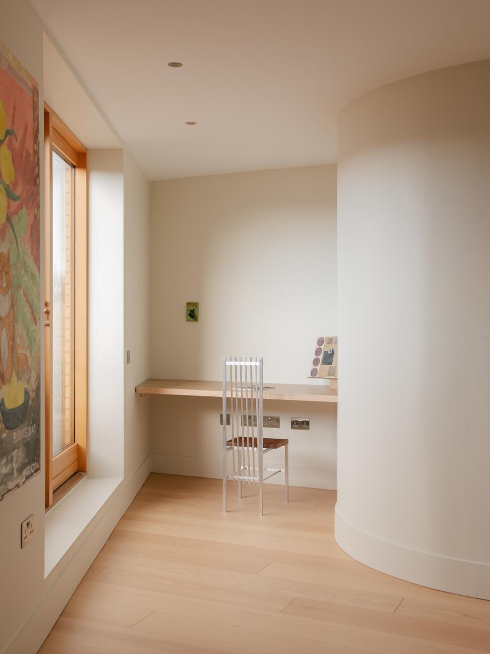 Curved plaster wall leading to a built-in desk by a timber window